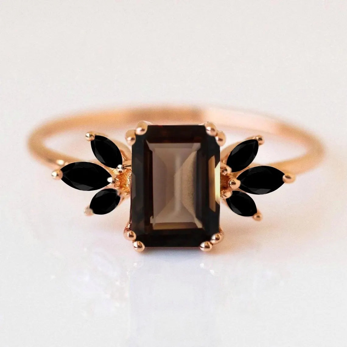 Gold ring with a central black gemstone and leaf-shaped stones on a white background